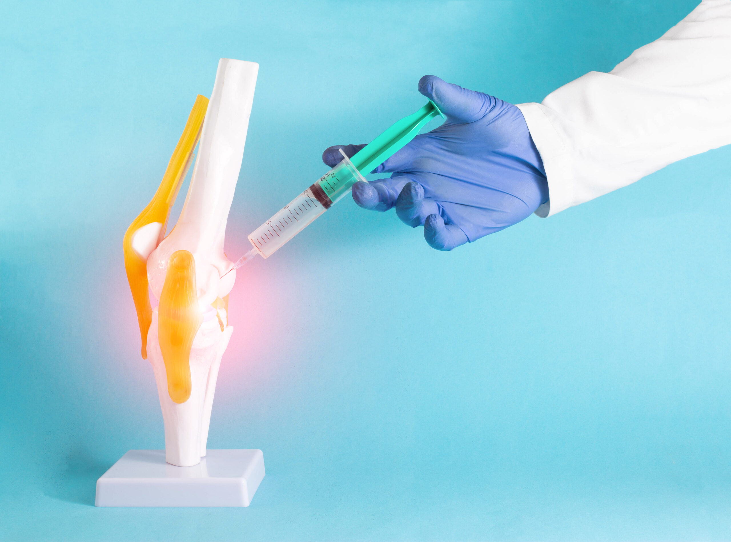 The doctor makes a therapeutic injection into the mock knee joint with corticosteroid and ozone. Concept for the treatment of knee joints using injection blockade. Blue background, copy space for text